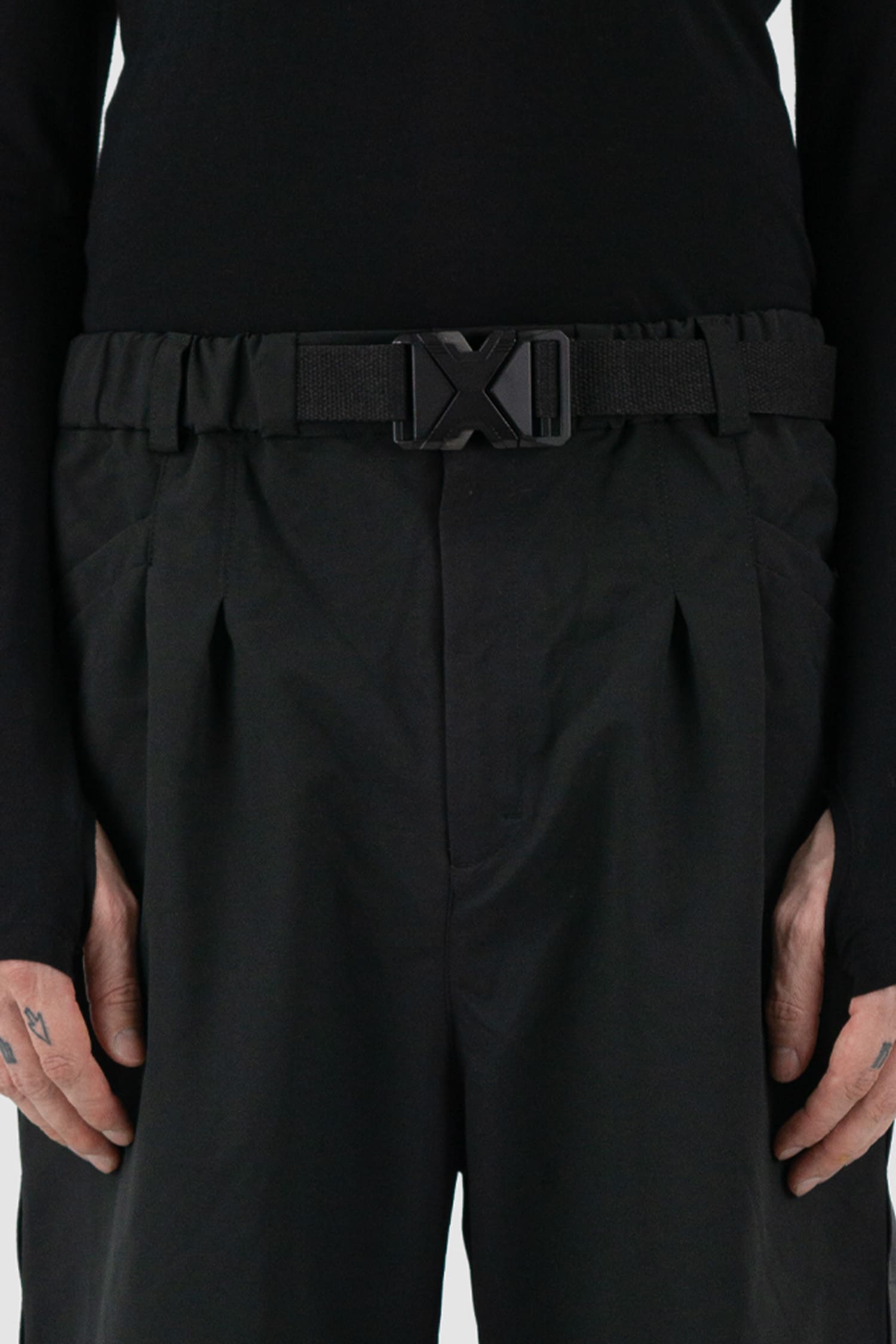 First Aid to the Injured - belt detail view of black belted utility pants with side straps for men from the FW24 collection feature an integrated snap belt and an elasticated parachute hem fastening.