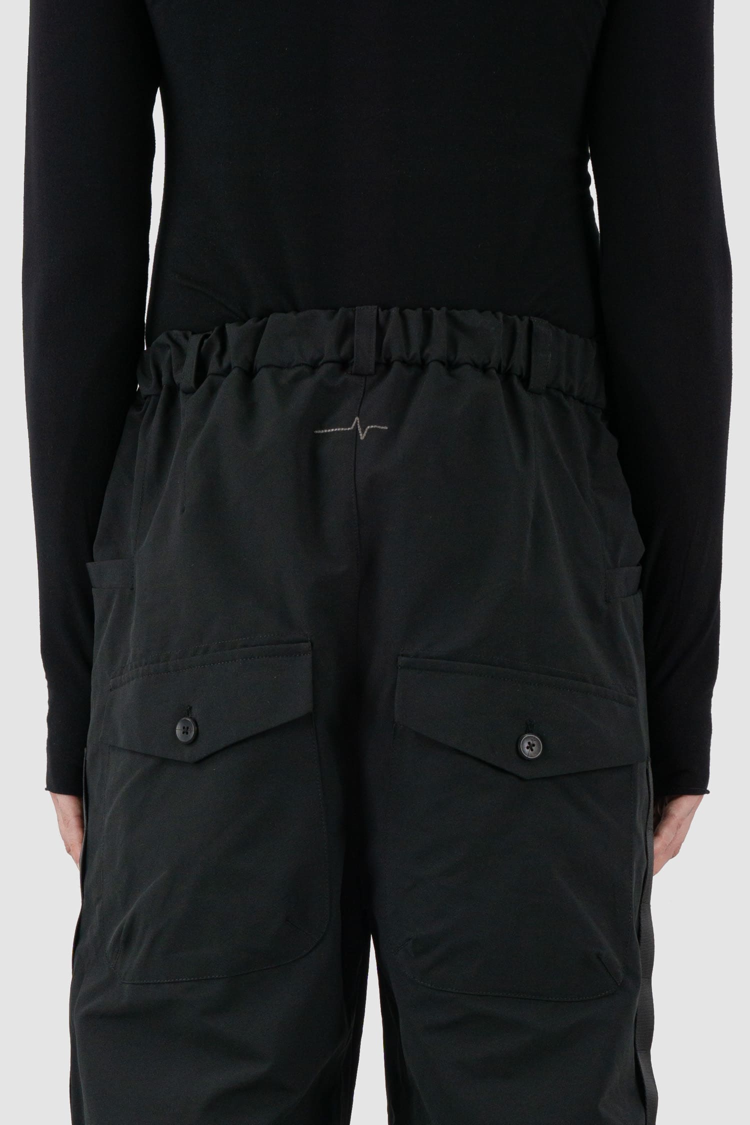 First Aid to the Injured - back detail of black belted utility pants with side straps for men from the FW24 collection feature an integrated snap belt and an elasticated parachute hem fastening.
