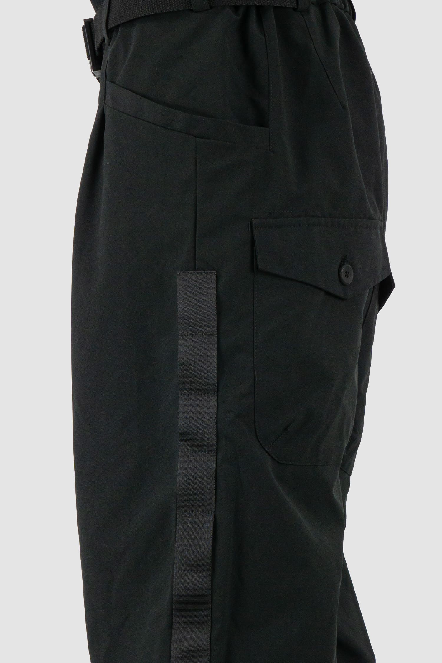 First Aid to the Injured - side detail view of black belted utility pants with side straps for men from the FW24 collection feature an integrated snap belt and an elasticated parachute hem fastening.