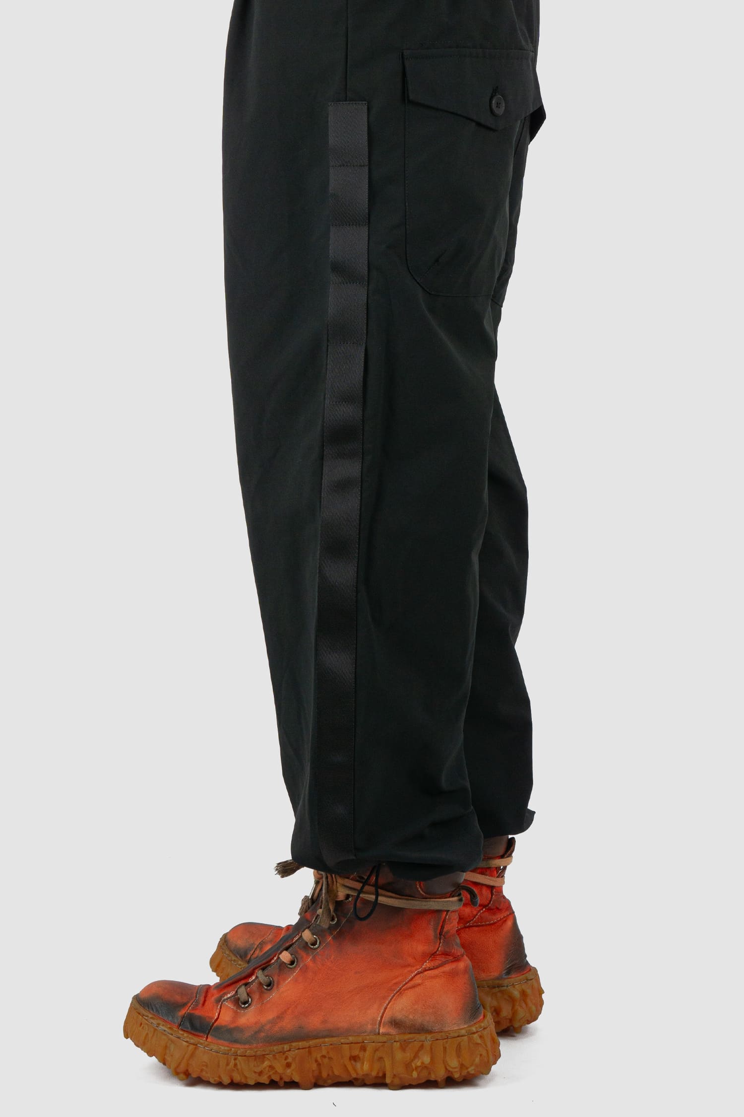 First Aid to the Injured - hem view of black belted utility pants with side straps for men from the FW24 collection feature an integrated snap belt and an elasticated parachute hem fastening.