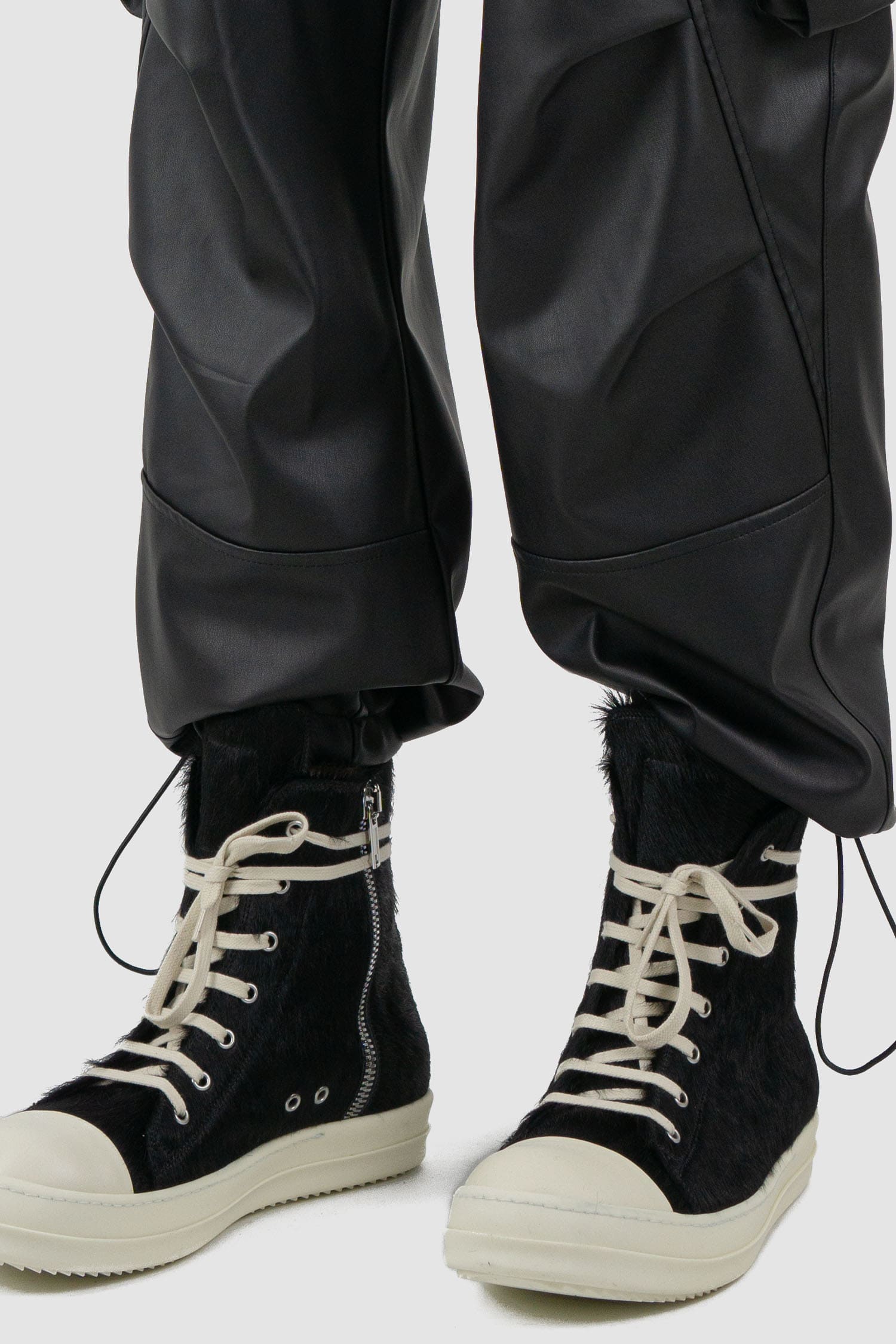 La Haine Inside Us - Front hem view of black men's vegan leather cargo pants with belt loops, adjustable drawstring at bottom hem, FW24 collection.