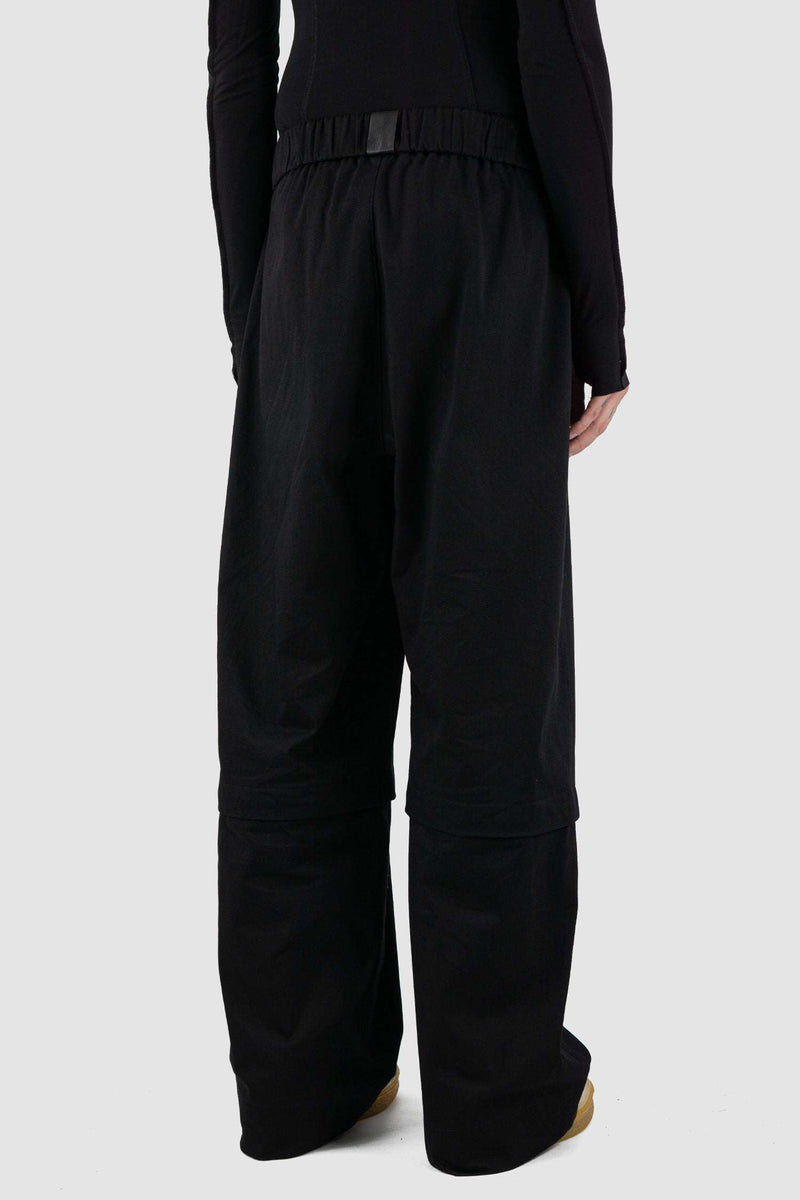 UY STUDIO Black Cotton Zipped Transform Pants: SS24 Collection, wide-legged, loose fit, black. Composition: 97% Cotton, 3% Elastane. Features hidden side seam pockets. Medium-weight fabric with a smooth touch. Detachable lower leg section for over knee shorts. Visible vegan leather UY label on the back.