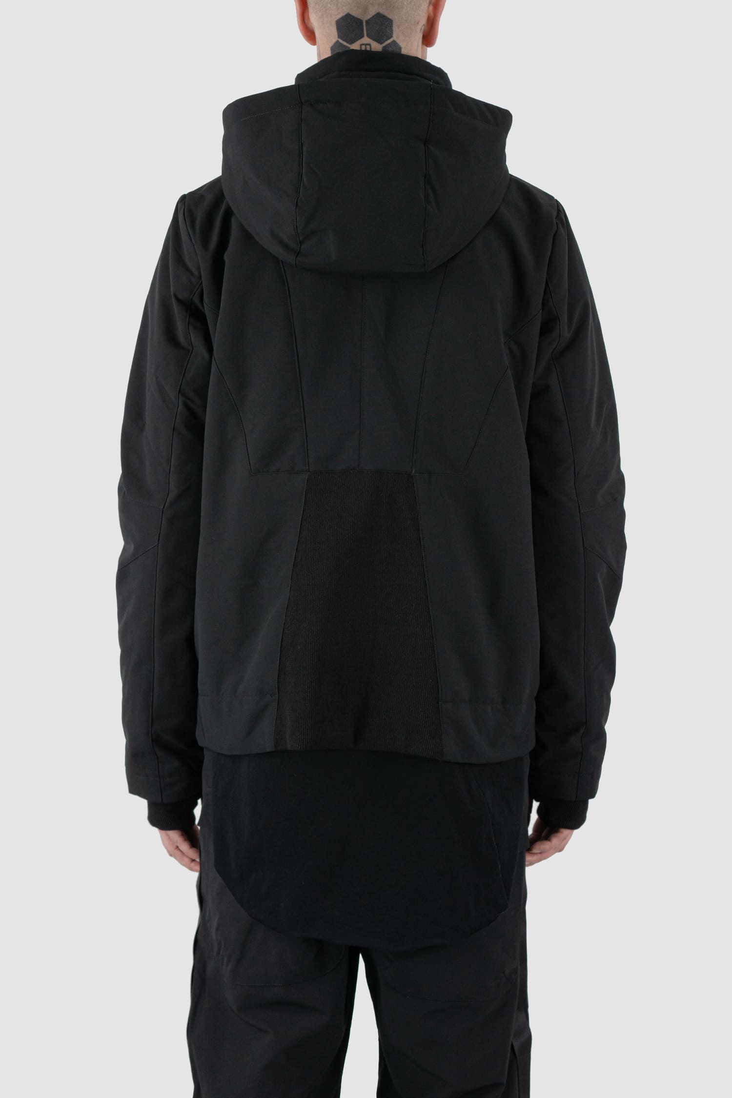 First Aid to the Injured - back view of black padded jacket with double zipper closure for men from the FW24 collection with detachable hood, 2 long zippers to close the jacket and knitted-in cuffs with thumb holes.