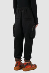 First Aid to the Injured - back side view of black tactical cargo joggers with side zip pockets for men from the FW24 collection with semi low crotch design, American fleece and spacious zipper pockets.