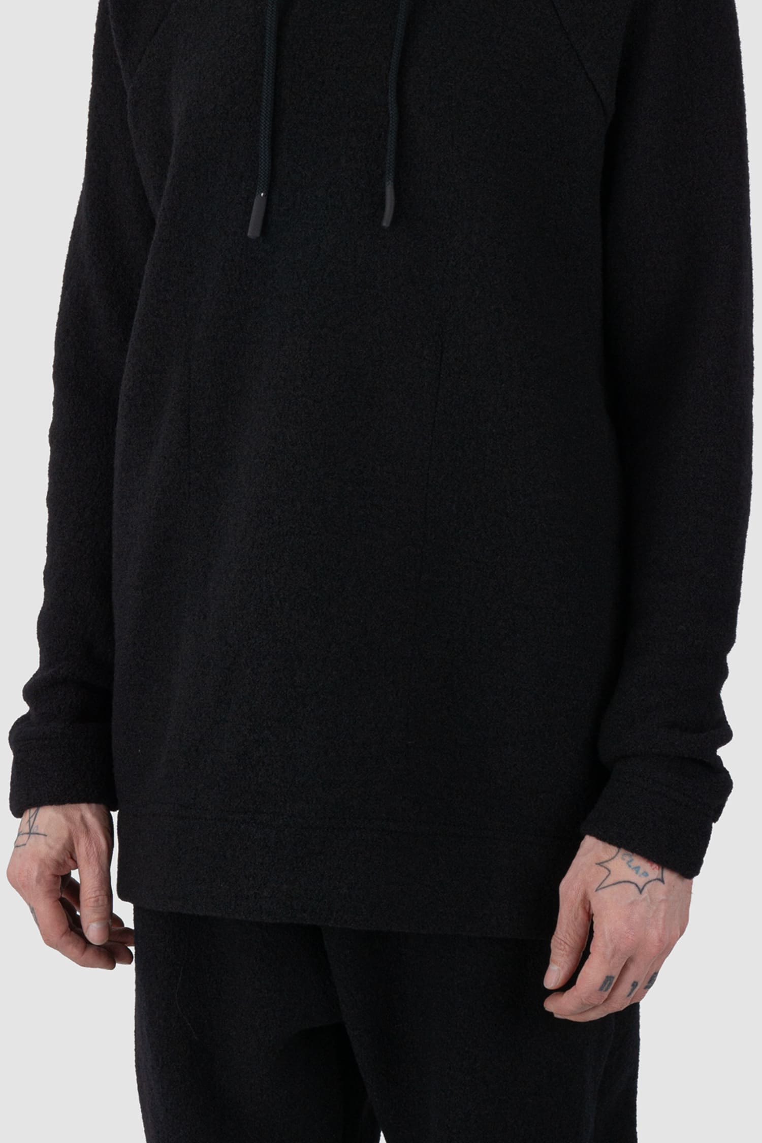 Nomen Nescio - front arm view of black recycled wool hoodie 518 for men from the FW24 collection offers a roomy fit with a large hood and wool rib details on the hem and cuffs.