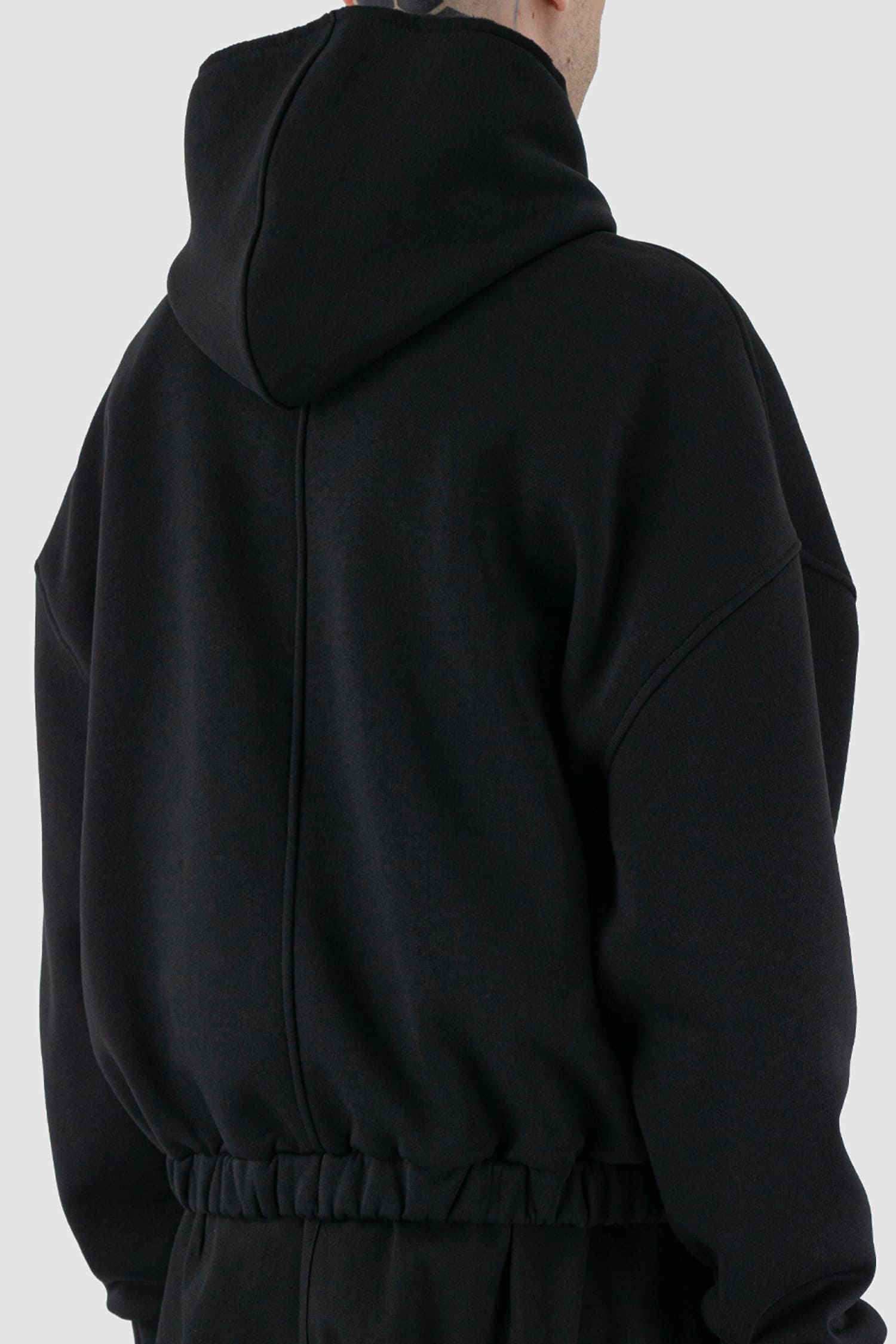 UY Studio - back detail view of black convertible oversized hooded sweater for men from the FW24 collection with semi-raglan shoulders, a large hood and a tight-fitting, flexible belly section.