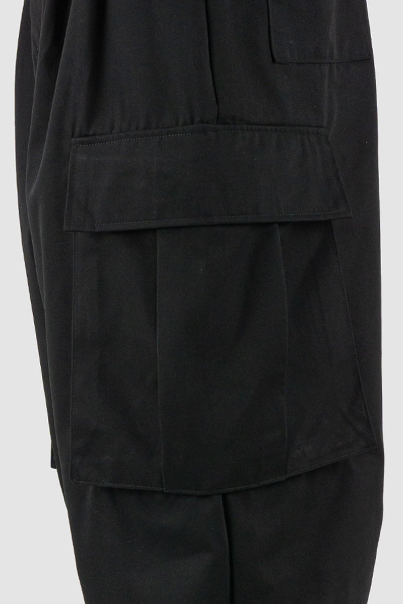 XConcept - pocket view of black shortened military cargo pants for men with cropped carrot cut, two huge cargo pockets on the sides, FW24 Collection.